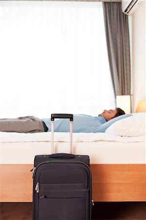 simsearch:693-07672684,k - Side view of young businessman sleeping in bed by luggage at hotel Stock Photo - Premium Royalty-Free, Code: 693-07672665