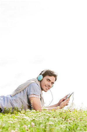 simsearch:693-07672615,k - Side view portrait of man listening to music on MP3 player using headphones in park against clear sky Stock Photo - Premium Royalty-Free, Code: 693-07672789