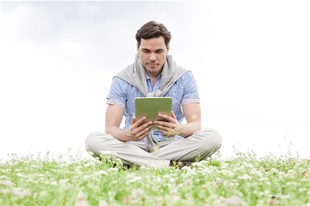 simsearch:693-07542313,k - Full length of young man holding digital tablet while sitting on grass against sky Stock Photo - Premium Royalty-Free, Code: 693-07672828