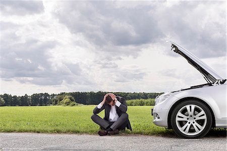 Full length of businessman with hands on head sitting by broken down car at countryside Stock Photo - Premium Royalty-Free, Code: 693-07672846