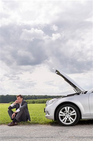 Full length of unhappy young businessman sitting by broken down car at countryside Stock Photo - Premium Royalty-Free, Code: 693-07672847