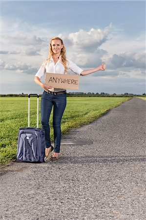 empty suitcase - Full length of woman hitching while holding anywhere sign on countryside Stock Photo - Premium Royalty-Free, Code: 693-07672861