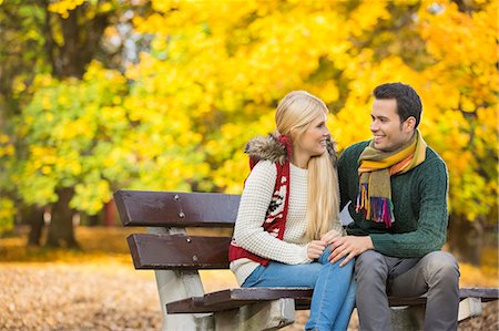 fall outdoors couple - Happy young couple looking at each other while sitting on park bench during autumn Stock Photo - Premium Royalty-Free, Code: 693-07672915