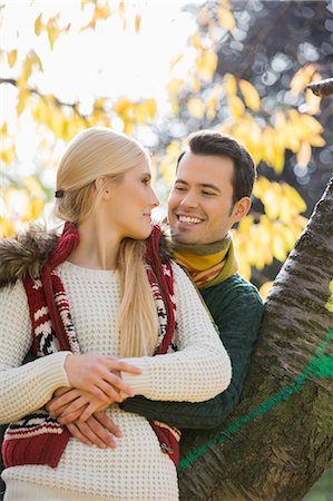 simsearch:693-07672684,k - Happy young man hugging woman while leaning on tree trunk during autumn in park Stock Photo - Premium Royalty-Free, Code: 693-07672910