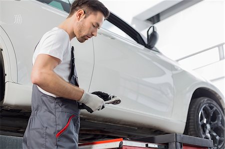 simsearch:693-07672925,k - Side view of repairman holding tool while standing by car in workshop Foto de stock - Sin royalties Premium, Código: 693-07672951