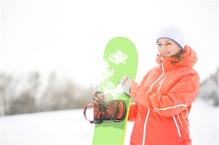 sports and snowboarding - Happy young woman looking away while holding snowboard in snow Stock Photo - Premium Royalty-Free, Code: 693-07673074