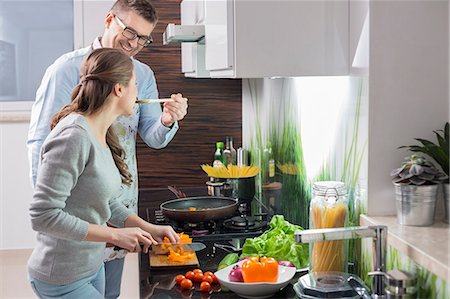 Happy man feeding food to woman cutting vegetables in kitchen Stock Photo - Premium Royalty-Free, Code: 693-07673262