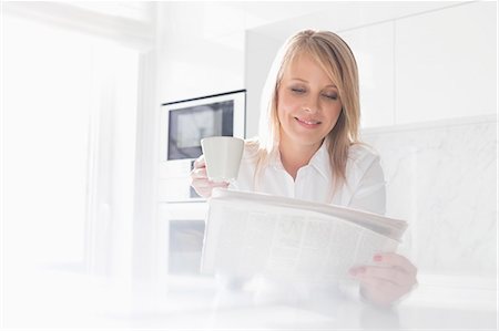 Happy mid adult businesswoman having coffee while reading newspaper at home Stock Photo - Premium Royalty-Free, Code: 693-07912359