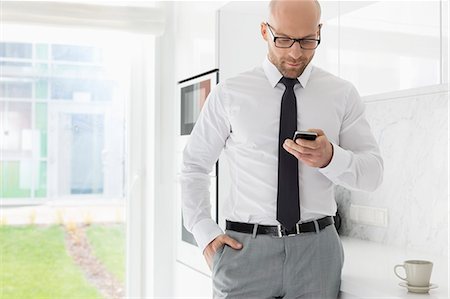 Mid adult businessman text messaging through smart phone at home Stock Photo - Premium Royalty-Free, Code: 693-07912351