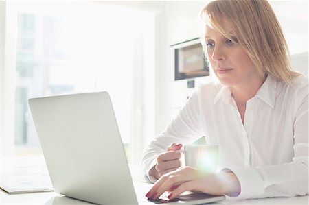 simsearch:693-07542313,k - Beautiful mid adult businesswoman using laptop while having coffee at home Stock Photo - Premium Royalty-Free, Code: 693-07912361