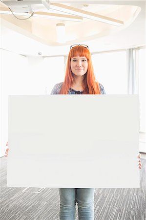 Portrait of confident businesswoman holding blank placard in creative office Fotografie stock - Premium Royalty-Free, Codice: 693-07912495