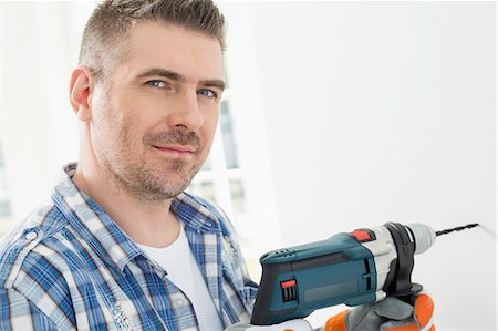 drilling (activity) - Portrait of mid-adult man drilling hole in wall Stock Photo - Premium Royalty-Free, Code: 693-07912590