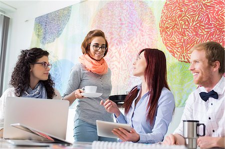 Businesswoman giving coffee to female colleague in creative office Stock Photo - Premium Royalty-Free, Code: 693-07912978