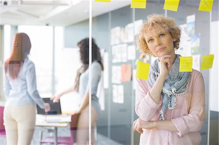 Thoughtful businesswoman reading sticky notes on glass with colleagues in background Foto de stock - Sin royalties Premium, Código: 693-07913041