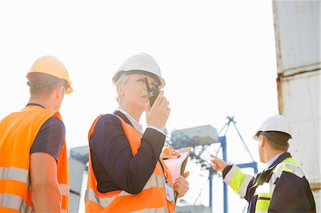 Female supervisor using walkie-talkie while workers discussing in background at shipyard Stock Photo - Premium Royalty-Free, Code: 693-07913144