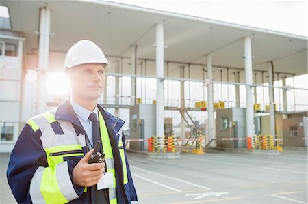Middle-aged male worker holding walkie-talkie while looking away in shipping yard Stock Photo - Premium Royalty-Free, Code: 693-07913166