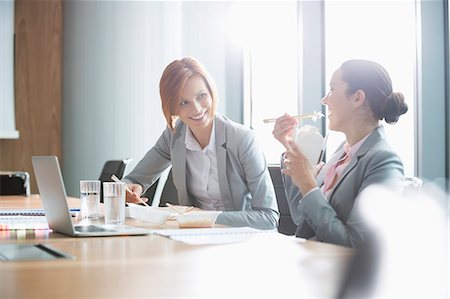 Smiling young businesswomen having lunch at table in office Stock Photo - Premium Royalty-Free, Code: 693-07913242