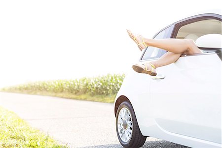 Low section of woman relaxing in car on country road against clear sky Stock Photo - Premium Royalty-Free, Code: 693-08127056
