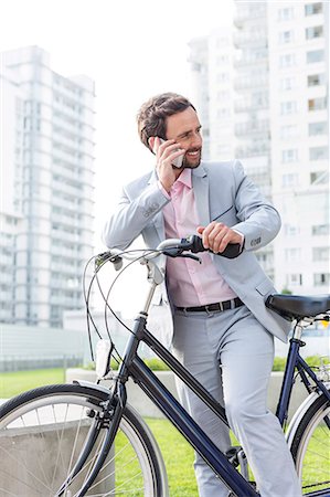 Businessman answering mobile phone while standing with bicycle outdoors Stock Photo - Premium Royalty-Free, Code: 693-08127177