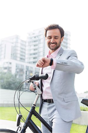 schedule - Happy businessman with bicycle checking time outdoors Stock Photo - Premium Royalty-Free, Code: 693-08127180