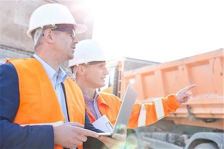 Supervisor showing something to colleague holding laptop at construction site Stock Photo - Premium Royalty-Free, Code: 693-08127744