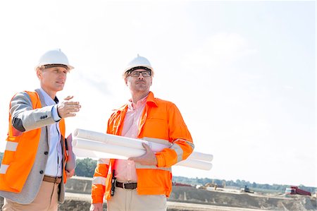 Supervisors with blueprints discussing at construction site against clear sky Stock Photo - Premium Royalty-Free, Code: 693-08127786