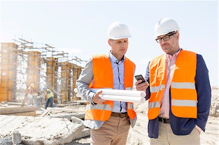 safety documents - Male engineers using mobile phone at construction site against clear sky Stock Photo - Premium Royalty-Free, Code: 693-08127805