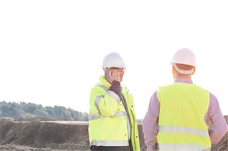 Male engineer using mobile phone while standing with colleague at construction site against clear sky Stock Photo - Premium Royalty-Free, Code: 693-08127833