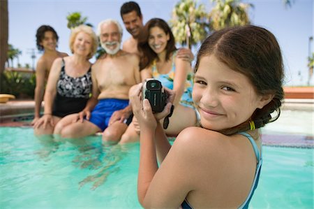 preteen girls looking older - Girl (10-12) in swimming pool, video taping brother (13-15), parents, and grandparents, portrait. Stock Photo - Premium Royalty-Free, Code: 693-03299419