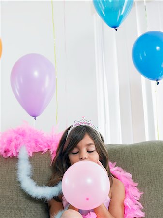 simsearch:693-03305634,k - Young girl (7-9) sitting on sofa, blowing up balloon Stock Photo - Premium Royalty-Free, Code: 693-03305635