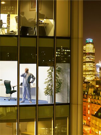 Man wearing pajamas standing in office and yawning, view from building exterior Stock Photo - Premium Royalty-Free, Code: 693-03305995