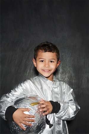 Portrait of young boy (5-6) in astronaut costume, holding helmet, smiling, studio shot Stock Photo - Premium Royalty-Free, Code: 693-03307214