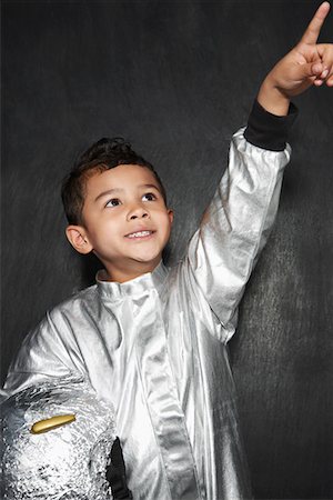 silver astronaut images - Portrait of young boy (5-6) in astronaut costume, pointing upwards, smiling, studio shot Stock Photo - Premium Royalty-Free, Code: 693-03307215