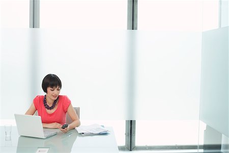 Woman using mobile phone and laptop in modern cubicle Stock Photo - Premium Royalty-Free, Code: 693-03307886