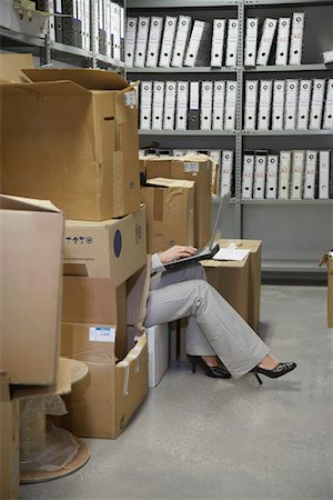 Woman using laptop, sitting on floor between boxes in storage room, low section Stock Photo - Premium Royalty-Free, Code: 693-03307954