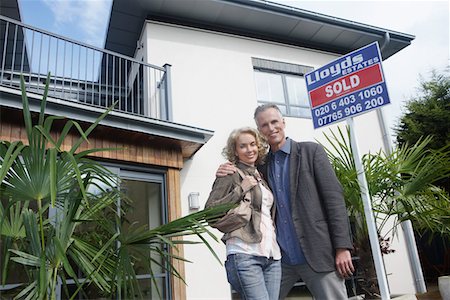 sold sign - Couple embracing outside new home with sold sign, portrait Stock Photo - Premium Royalty-Free, Code: 693-03308233