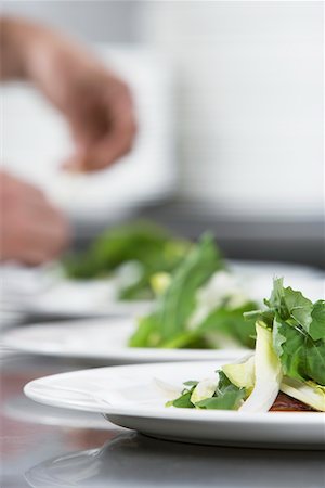 plated food - Chef preparing meal, focus on salad in foreground Stock Photo - Premium Royalty-Free, Code: 693-03308930