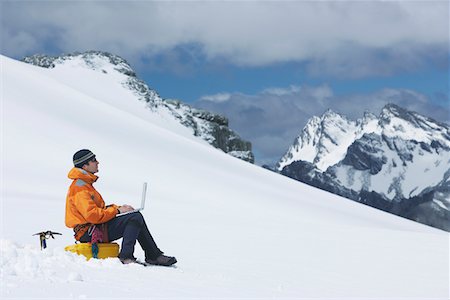 Hiker using laptop on snowy mountain peak Stock Photo - Premium Royalty-Free, Code: 693-03300931