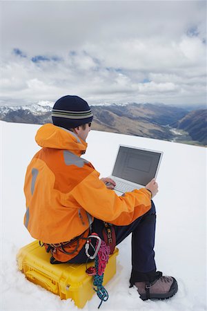 Hiker using laptop on snowy mountain peak, back view Stock Photo - Premium Royalty-Free, Code: 693-03300932