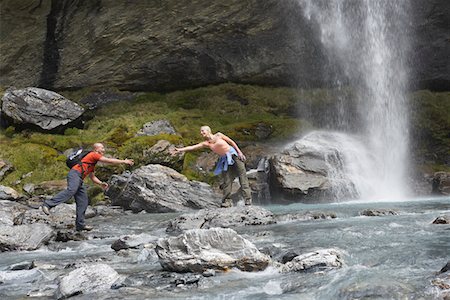 Hiker extending arm to another hiker under a waterfall Stock Photo - Premium Royalty-Free, Code: 693-03300996