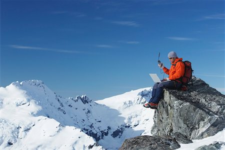 Mountain climber using laptop with walkie-talkie on mountain peak Stock Photo - Premium Royalty-Free, Code: 693-03300992