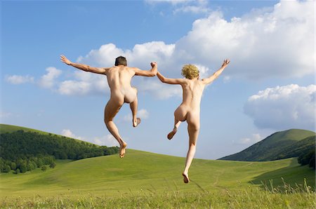 Young naked couple running and jumping in mountain field, back view, low angle view Stock Photo - Premium Royalty-Free, Code: 693-03301628