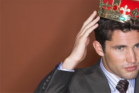 Man putting on crown against brown background, close-up Stock Photo - Premium Royalty-Free, Code: 693-03303800