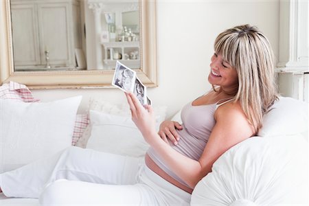 Pregnant woman sitting on sofa with baby scan photos Stock Photo - Premium Royalty-Free, Code: 693-03317755