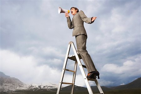 pantsuit - Businesswoman on ladder in mountain field shouting Through Megaphone, low angle view Stock Photo - Premium Royalty-Free, Code: 693-03557158