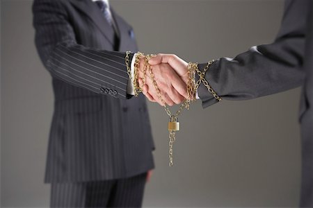 Businessmen shaking hands wrapped in gold chain with padlock, mid section Stock Photo - Premium Royalty-Free, Code: 693-03565266