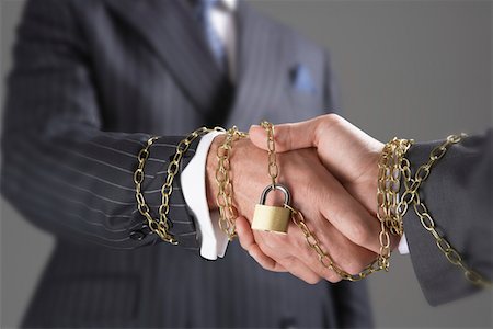 Businessmen shaking hands wrapped in gold chain with padlock, close-up of hands Stock Photo - Premium Royalty-Free, Code: 693-03565267