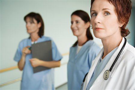 Serious Physician with Nurses in hospital corridor, focus on physician, portrait Stock Photo - Premium Royalty-Free, Code: 693-03565435