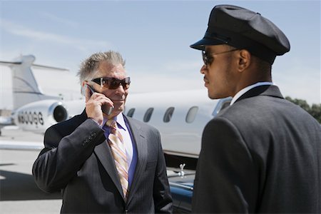 Senior businessman standing outside private jet and talking on phone, Chauffeur assisting. Stock Photo - Premium Royalty-Free, Code: 693-03707195