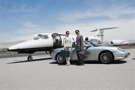 Mid-adult businesswoman and mid-adult businessman standing in front of convertible and private jet on landing strip. Stock Photo - Premium Royalty-Free, Code: 693-03707193